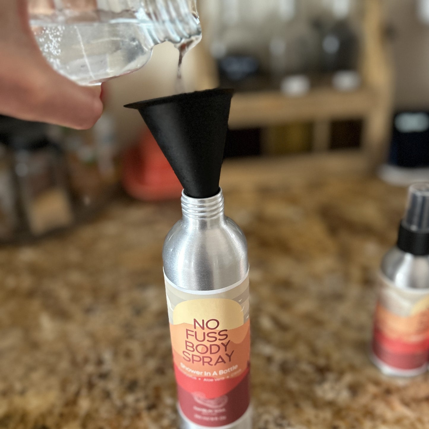 Refill spray going into funnel that is placed in aluminum spray bottle