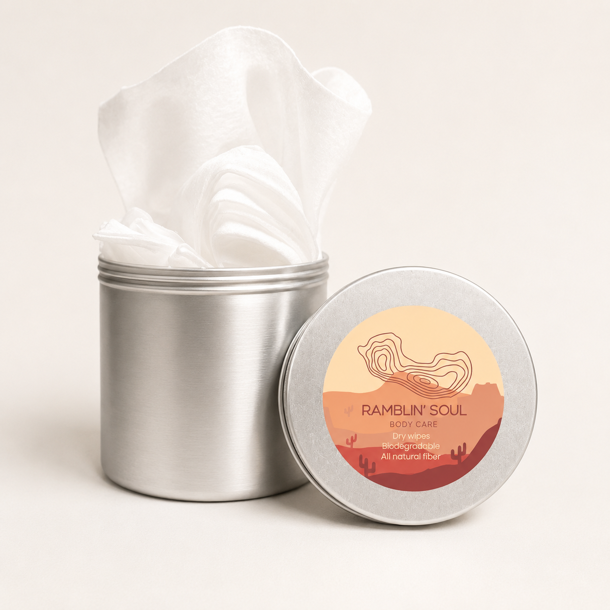 A silver metal tin of Ramblin' Soul Body Care cotton pads with white pads partially pulled out, alongside the round silver lid featuring a desert landscape label.