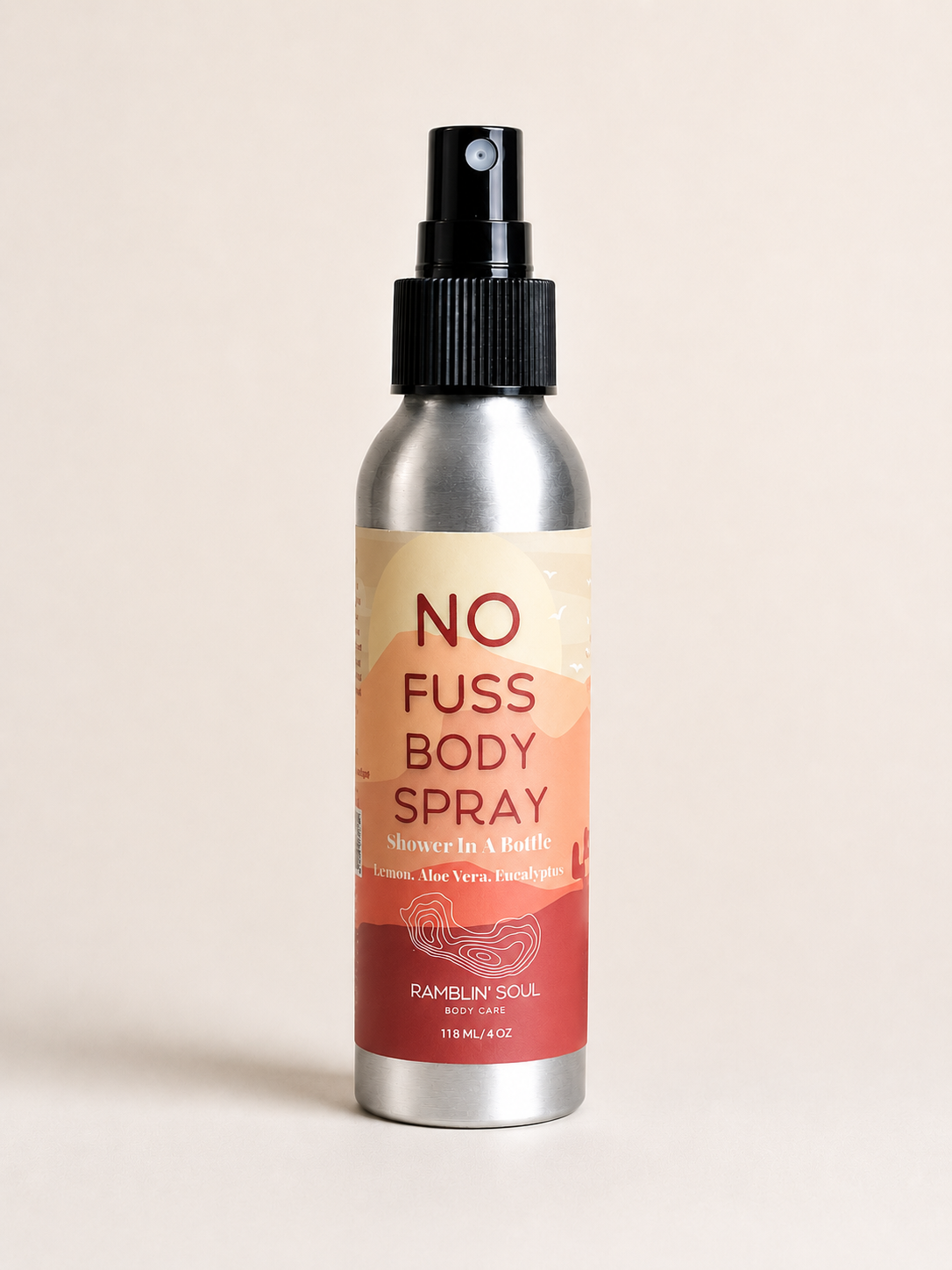 A silver aluminum spray bottle of Ramblin Soul No Fuss Body Spray with a black spray nozzle and a beige-to-red label, set against a solid light beige background.