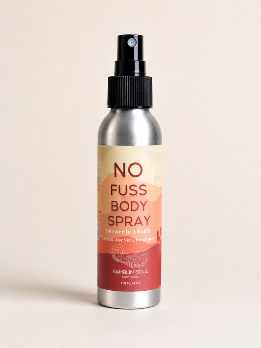 A silver aluminum spray bottle of Ramblin Soul No Fuss Body Spray with a black spray nozzle and a beige-to-red label, set against a solid light beige background.