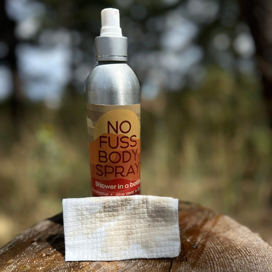 A bottle of No Fuss Body Spray and a dry wipe showing dirt wiped off after using spray.